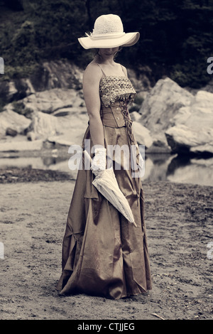 a young woman in a romantic period dress standing on the shore of a lake Stock Photo