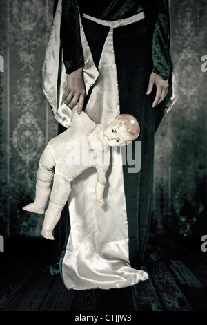 a woman in a period dress holding an old, broken doll in her hand Stock Photo