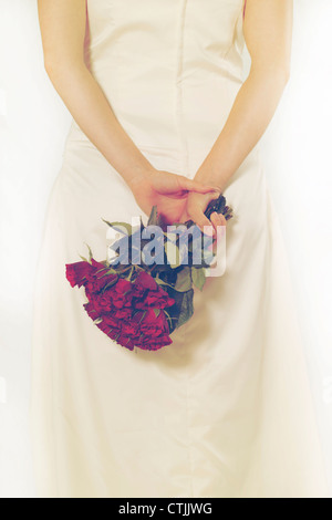 a woman in a white dress holding a bouquet of roses behind her back Stock Photo