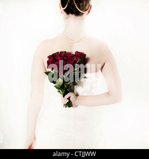 a woman in a white dress holding a bouquet of roses behind her back Stock Photo