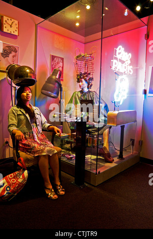 Young Asian woman sitting in chair under hairdresser display hair dryer Museum of Vancouver Stock Photo