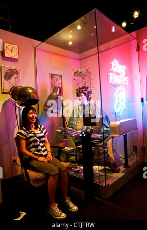 Young Asian woman sitting in chair under display hair dryer Museum of Vancouver Stock Photo