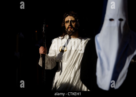 A masked man dressed as Jesus Christ walks near a penitent during an Easter Holy Week procession in Puente Genil, Spain Stock Photo