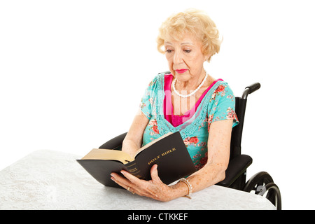 Disabed senior woman in wheelchair, reading her bible. Isolated on white.  Stock Photo