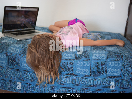 Seven year old girl laying in bed watching a movie on a laptop computer. Stock Photo