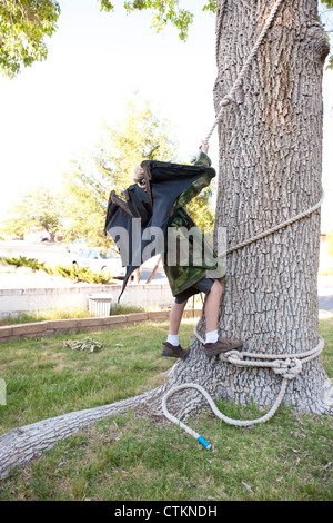 Eight year old boy pretending to be Batman, climbing a tree using a rope. Stock Photo