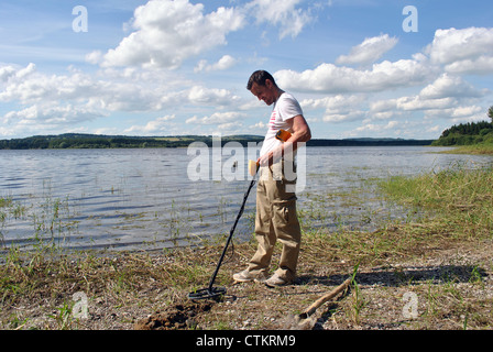 man on a lakeshore with a metal detector Stock Photo