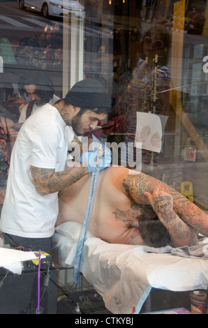 Canada, Ontario, Toronto. Tattoo artist in downtown window applying ink to client. Stock Photo