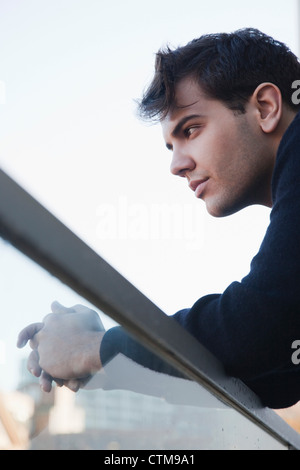 Handsome and thoughtful young man leaning on glass railing of a balcony Stock Photo