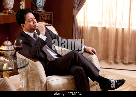 Mature businessman enjoying cigar and wine in a luxurious room Stock Photo