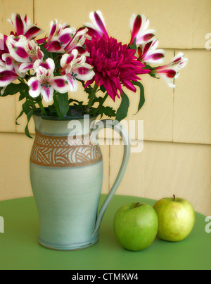 Red and white flowers (azaleas) in a vase on a table beside green apples, Vermont USA Stock Photo