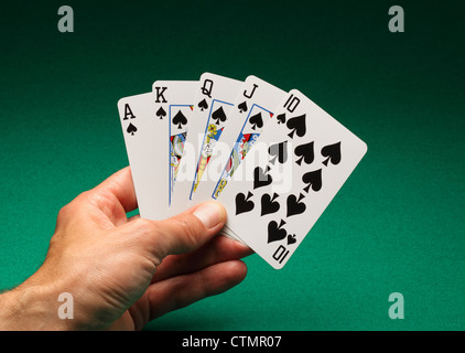 A man's hand holding playing cards on a green table. A Royal Flush of spades in the game of Poker Stock Photo