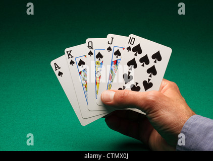 A man's hand holding playing cards on a green table. A Royal Flush of spades in the game of Poker Stock Photo