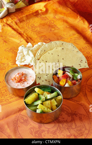 Indian cooking. Carrot raita, cucumber relish, fresh tomato and onion salad / kachoomer with paapri and pappadums Stock Photo