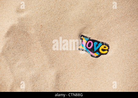 Multicoloured embroidery iron on LOVE patch in sand on a beach Stock Photo