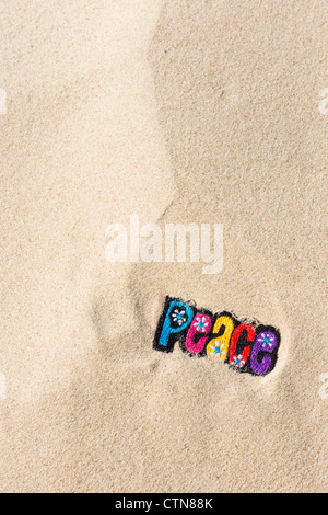 Multicoloured embroidery iron on PEACE patch in sand on a beach Stock Photo