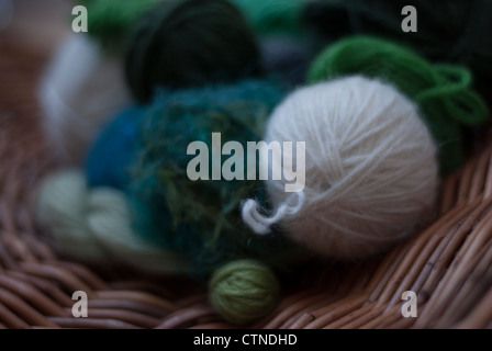 Balls of wool in shades of green, blue and white and on circular willow basket weave Stock Photo