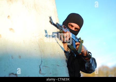 terrorist with mask hidden behind a wall and aiming with his gun Stock Photo