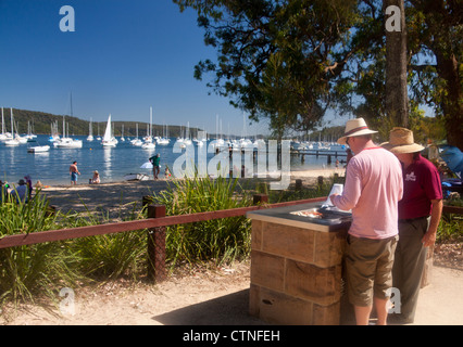 Typical Australian beach barbecue / barby with two men frying bacon and mushrooms Clareville Pittwater Sydney NSW Australia Stock Photo