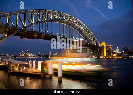 Ferry departing Milsons Point wharf at night with Harbour Bridge and Opera House in background Sydney New South Wales Australia Stock Photo