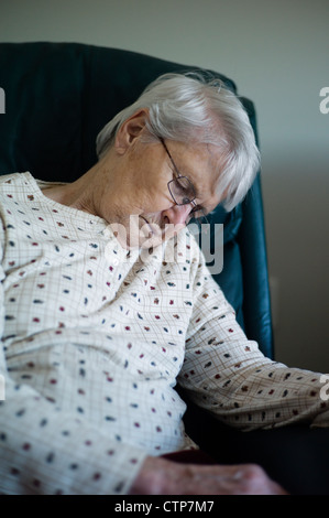 Old woman slumped over asleep in chair Stock Photo