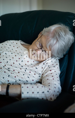 Old woman slumped over asleep in chair Stock Photo