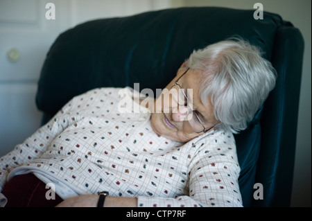 Old woman slumped over asleep in chair Stock Photo