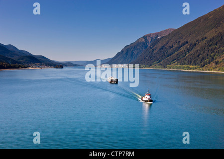 Aerial view tugboat towing cargo ship out Lynn canal Mount Roberts downtown Juneau in background Southeast Alaska Summer Stock Photo