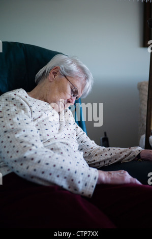 Old woman slumped over asleep in chair Stock Photo