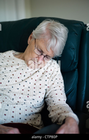 Old woman slumped over asleep in chair Stock Photo