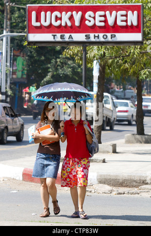 Teenage Burmese girls walk together under the shade of an umbrella in (Rangoon) Yangon, (Burma) Myanmar. Stock Photo