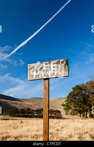 A hand painted sign on a wooden stick warning people of Deep Mud at a lake in a national park in Wales.  A jet trail above. Stock Photo