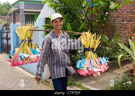 local villager in rural village street with childrens toys for sale hanging from bamboo over shoulder Stock Photo