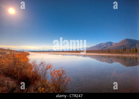 Northern Lights dancing over Alaska Range reflected in beaver pond along Parks Highway under full moon Broad Pass Southcentral Stock Photo