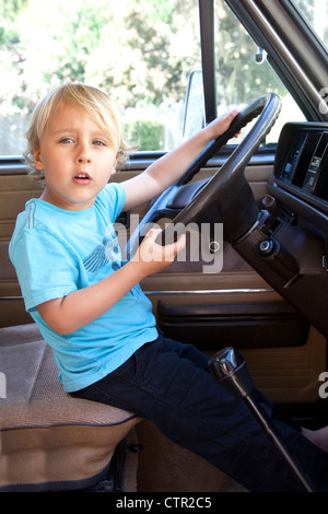 A little boy is behind a steering wheel pretending to drive. Stock Photo