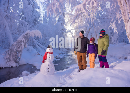 Family stands next snowman small stream in hoarfrost covered forest Russian Jack Springs Park Anchorage Southcentral Alaska Stock Photo