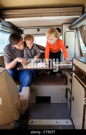 A father and his two sons are playing in the back of their camper trailer. Stock Photo