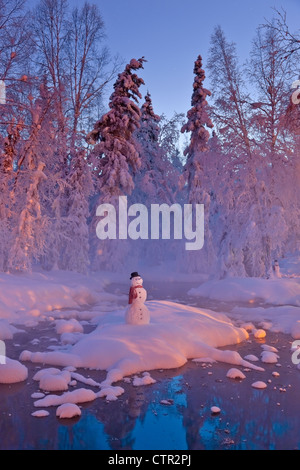 Snowman standing on small island in middle stream fog hoar frosted trees in background Russian Jack Springs Park Anchorage Stock Photo