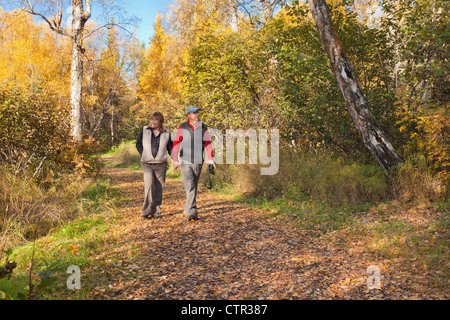 A middle age couple walk on a leaf covered path through a woodland park on a sunny afternoon in Anchorage, Alaska, Fall Stock Photo