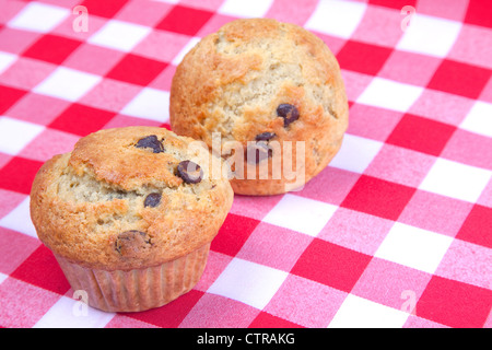 A pair of homemade banana chocolate chip muffins on a red gingham table cloth. Stock Photo