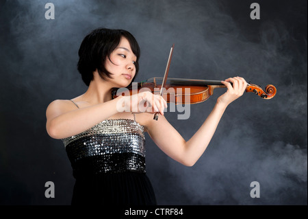 female asian violinist on a dark background with smoke Stock Photo