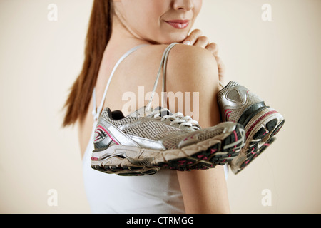 A young woman holding a pair of training shoes over her shoulder, close-up