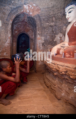 Myanmar, Burma. Bagan. Two Young Novice Monks Praying in front of Buddha Statue. Stock Photo