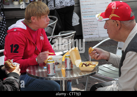Unhappy looking men eating junk food within Portsmouth open air market, England, UK Stock Photo