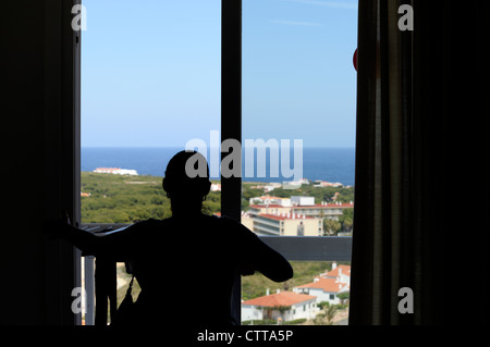 hotel room window with a female in silhouette against the outside view Stock Photo