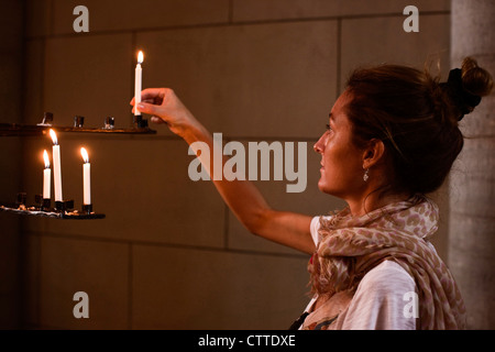 A woman places a lit candle on an iron candlebra in Uppsala's cathedral. Sweden. Stock Photo