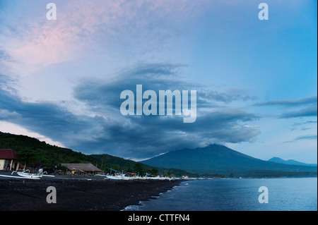 The great volcano Gunung Agung seen during a dramatic sunset on the Jemeluk beach in the Amed area of Bali, Indonesia. Stock Photo