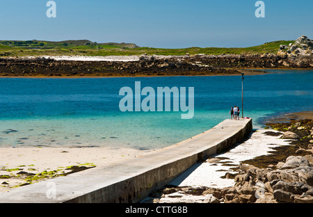 Lower Town Quay on St Martins Isles of Scilly with three people on the end in summer, West of England UK Stock Photo