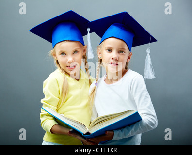 Portrait of lovely twin girls in hats with tassels holding open book Stock Photo