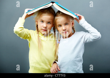 Portrait of lovely twin girls holding open book over heads Stock Photo